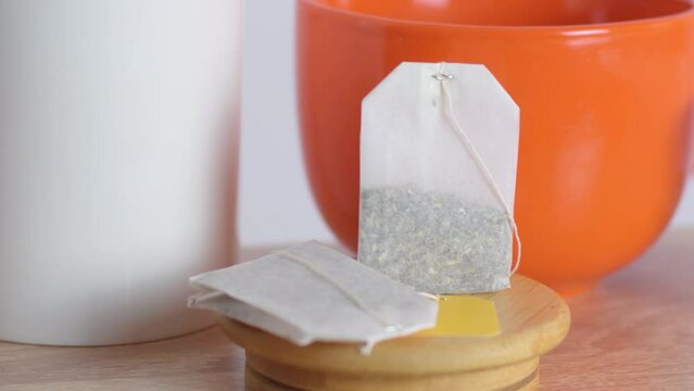 Tea bags on a wooden stand. A blank yellow label with no logos is displayed against a backdrop of large orange cups.