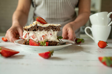 Piece of fresh chocolate strawberry cream cake with meringue topping. Served by a woman with apron 