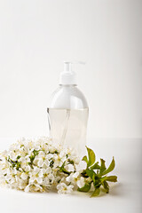 Transparent hand soap dispenser surrounded by fresh spring blossoms on white background, portraying hygiene and nature's touch. Shampoo, shower gel, body lotion. Natural organic cosmetics. Vertical