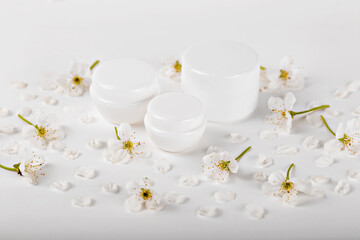 Mockup. Elegant white cosmetic jars surrounded by delicate cherry blossoms on pure white background, ideal for beauty and skincare themes. Natural organic cosmetics