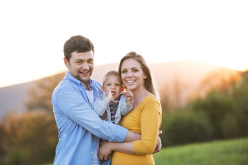 New parents holding small toddler, baby, outdoors in spring nature. Happy family moment