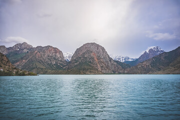 Panoramic view of blue Iskanderkul lake and rocky mountains in Tajikistan on a cloudy cloudy day