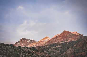 Rocky peaks of mountains and ridges illuminated by the bright orange sunset sun