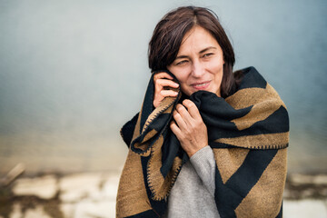 Portrait of beautiful mature woman with blanket around shoulders, standing by lake.