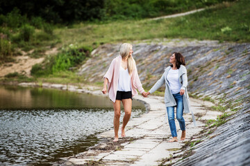 Adult daughter spending time with her mother. Mom and daughter outdoors, walking barefoot in water...