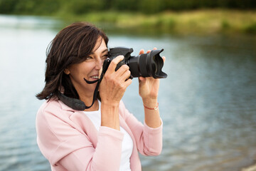 Portrait of beautiful mature woman on vacation, taking photos with professional camera, capturing...