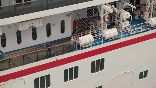 Liferaft station on cruise ship open deck. Washerman in protective overalls washes shipboard with pressure washer