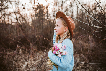 Portrait of a beautiful girl with a hat, holding bouquet of pink tulips. Spring moment, childhood...