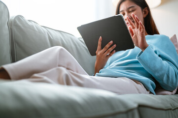 living, reading, social, internet, lady, communication, looking, computer, relaxation, sofa. A woman is sitting on a couch and using a tablet. She is smiling and she is enjoying herself.