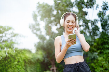 run, runner, sport, teen, exercise, fit, fitness, listening, message, workout. A woman is walking in a park while listening to music on her phone. She is smiling and she is enjoying herself.