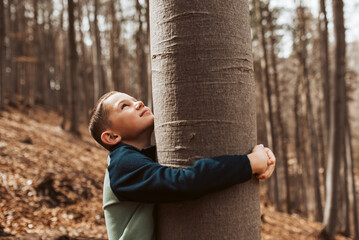 Cute boy on walk in forest, hugging tree, enjoying the peaceful moment, looking up at tree crown....