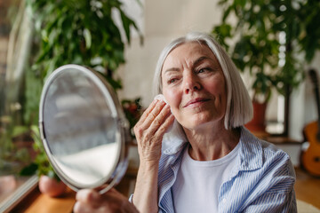 Skincare for mature woman. Portrait of beautiful older woman with gray hair cleaning, taking care...