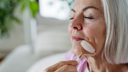 Skincare for mature woman. Older woman using facial roller for blood circulation, after serum.