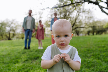 Portrait of cute baby boy standing in front of his family, walking outdoors in spring nature.