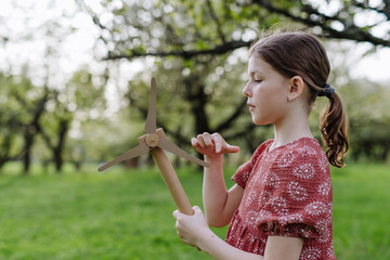 Girl standing outdoors in park, holding wind turbine. Renewable wind energy and sustainable lifestyle.