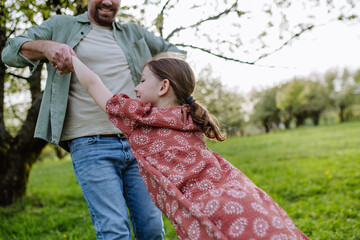Father spinning daughter around, holding her under armpits. Dad and girl having fun, laughing outdoor. Father's day concept.