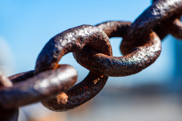 Rusty and heavily weathered old chain with massive chain links. Close-up of a forged anchor chain with selective sharpness and corroded surface. Silhouette with blurred background.