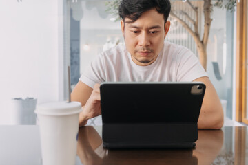 Front view of asian man using laptop, sitting and working at cafe. digital nomad and freelance concept.