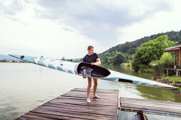 Young canoeist carry canoe and paddle, going into water, walking on wooden dock. Concept of...