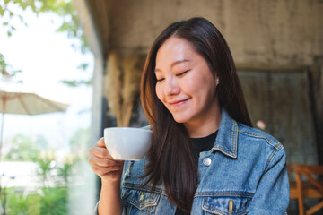 Portrait image of a beautiful young asian woman holding and drinking hot coffee in cafe