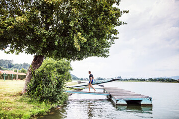 Young canoeist carry canoe and paddle, going into water, walking on wooden dock. Concept of...