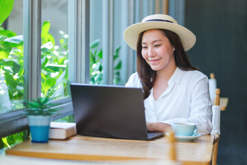 Portrait image of a young woman with hat working on laptop computer in cafe