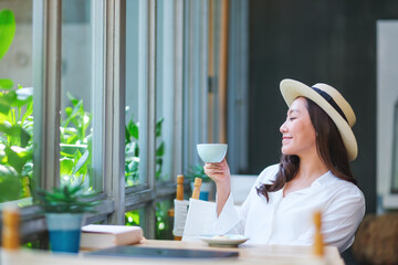 Portrait image of a beautiful young woman with hat drinking coffee and relaxing in cafe