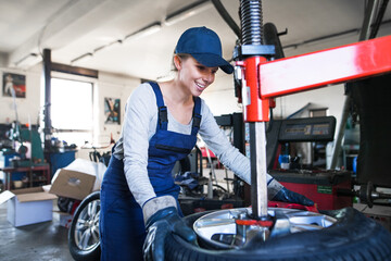 Female auto mechanic changing tieres in auto service, using machinery to removing tire. Beautiful...