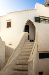 An example of a house from the picturesque and charming village of Binibeca with a black cat sitting on the staircase. Like the rest of the town, the house is whitewashed and has wooden doors and wind