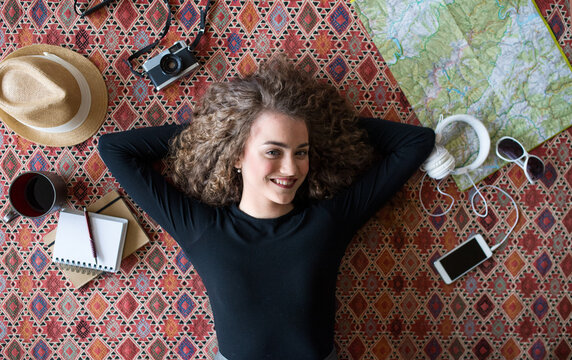 Woman planning summer vacation abroad, going on trip alone. Lying on carpet, daydreaming about adventures.