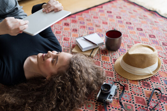 Woman planning summer vacation abroad, going on trip alone. Lying on carpet, daydreaming about adventures.