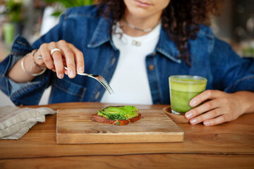 Woman enjoys avocado toast and green smoothie in a restaurant, showcasing vegan healthy food options
