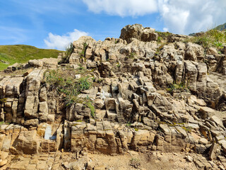 Rugged rock formation stands against the backdrop of a clear blue sky with fluffy white clouds....