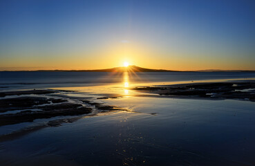 Long exposure image of sunrise over the crest of Rangitoto Island. Milford Beach. Auckland.