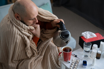 Top view of a man making tea sick at home suffering from high fever and headache. Medicine and healthcare