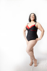 Obraz premium Portrait of attractive dreamy thick woman in red black swimsuit posing on white background. Body positive, photo shoot, selfie. Funny plus size model