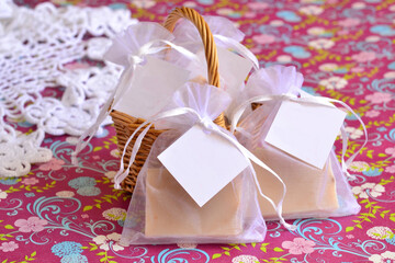 Summer retro wedding party favors small bag with handmade soap bar gift on pink colorful floral background with wicker and white lace doily, diy guest souvenir, vintage style event decoration