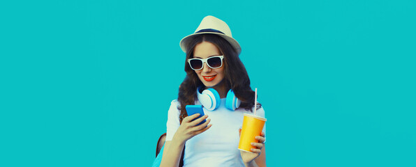 Portrait of modern young woman listening to music with headphones holding phone on blue background