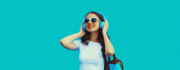 Happy modern happy young woman listening to music with headphones on blue background
