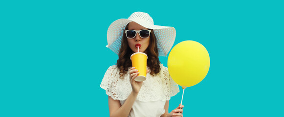 Beautiful young woman model with cup of juice holding yellow balloon summer hat on blue background