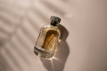 Golden perfume with leaf shadow on beige background, essential cosmetic product, romantic scent, spa elegance