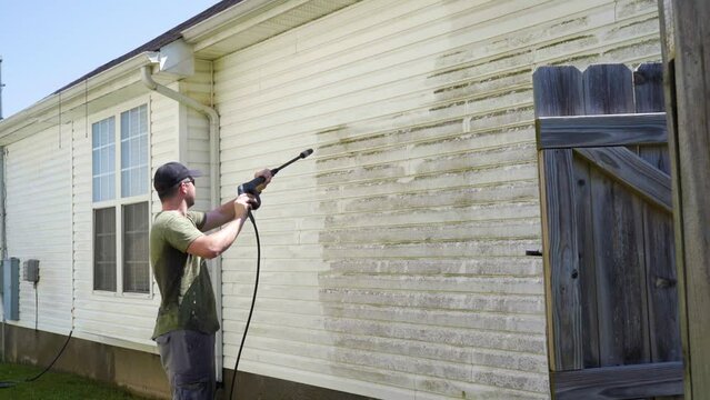 Pressure washing the side of a house. Wide shot.