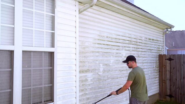 Homeowner sets down pressure washer while cleaning house. Wide shot