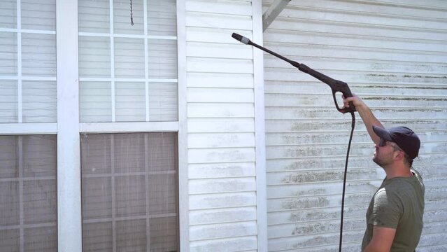 Homeowner pressure washes home siding summer day. Medium shot