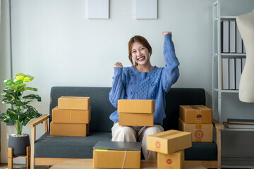 A woman is sitting on a couch with a pile of boxes in front of her. She is smiling and she is happy