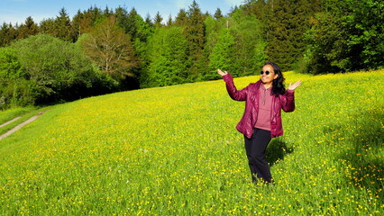 glückliche hübsche Asiatin steht lächelnd auf leuchtend grüner sonniger Wiese mit gelben...
