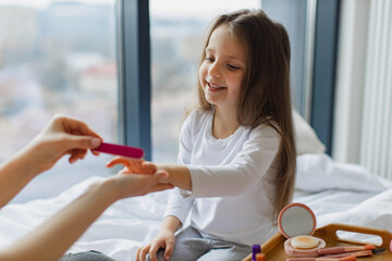 Mom uses a file to clean her cute daughter's nails before applying a manicure. Close-up view of...