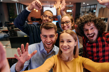 A diverse group of business professionals take a break from their tasks in a modern startup office to capture a creative selfie, showcasing teamwork and a vibrant workplace culture