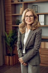 Woman psychotherapist in gray suit posing at her workplace in office