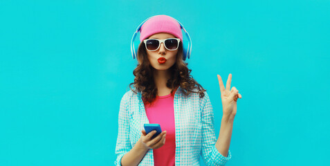 Portrait stylish modern young woman listening to music in headphones with phone on blue background